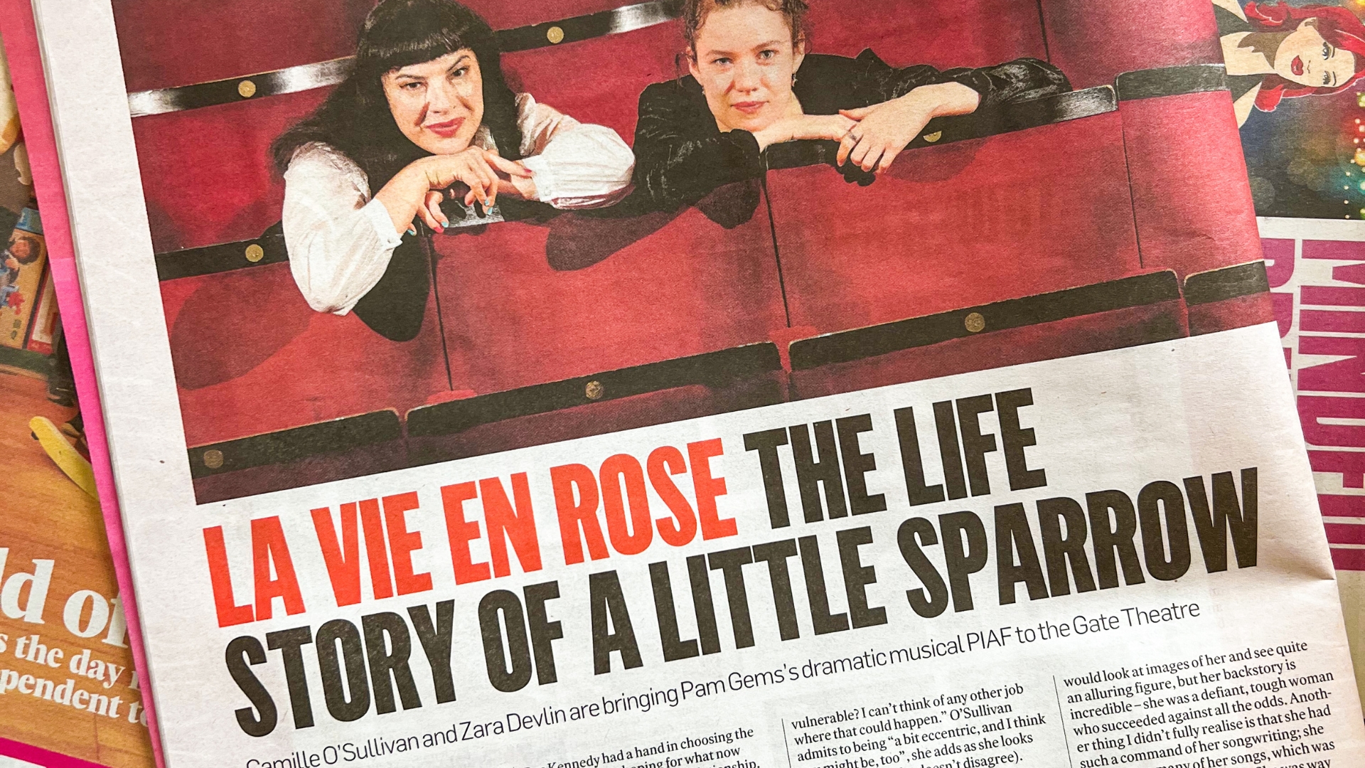 Photo of newspaper spread of Camille O Sullivan and Zara Develin sat side by side in the red seats of the Gate Theatre auditorium.